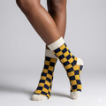 Checkered socks with yellow and navy pattern worn by a person on a light gray background